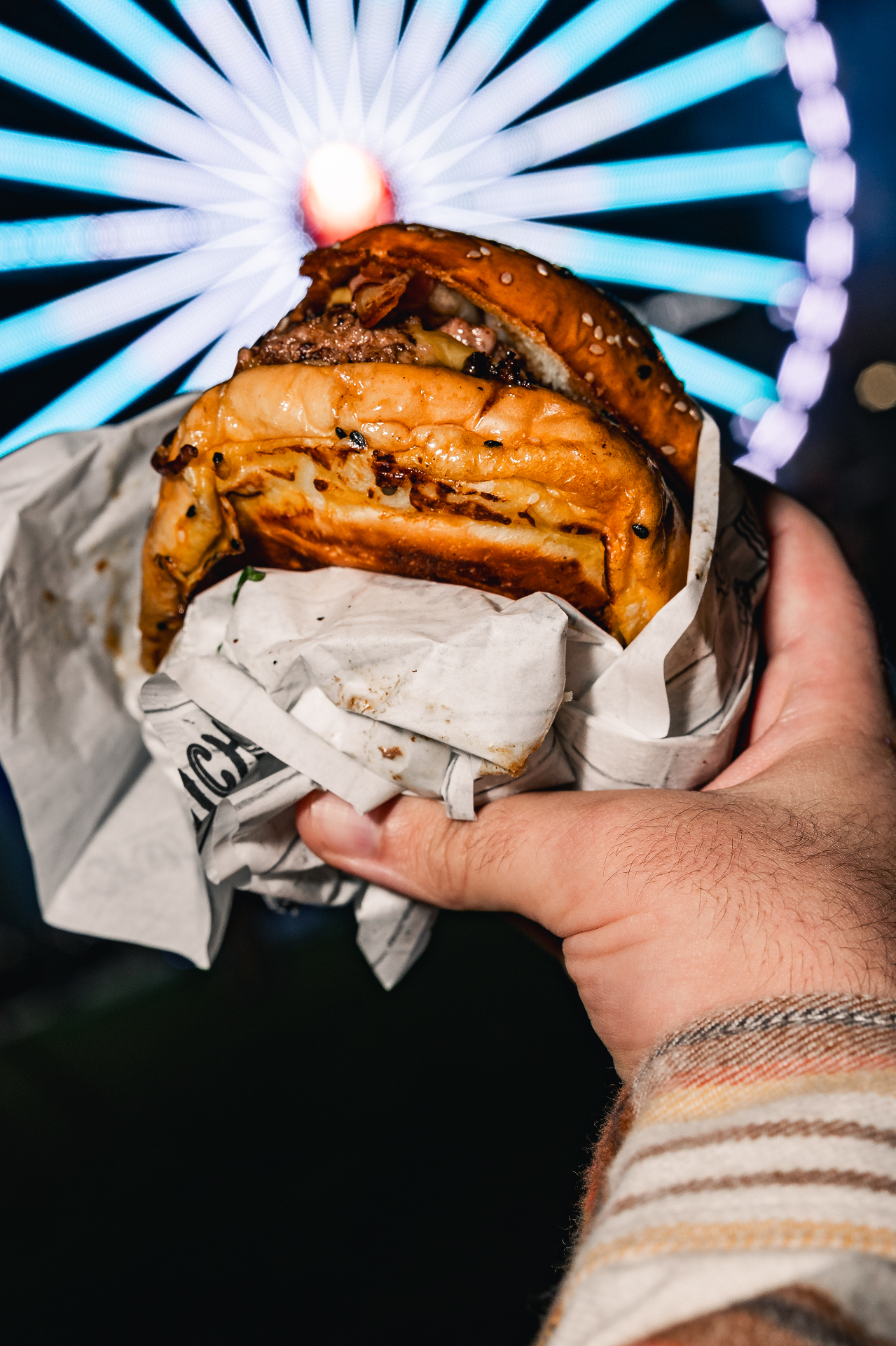 Hambúrguer Crunchy's segurado em frente a uma roda gigante iluminada num festival à noite