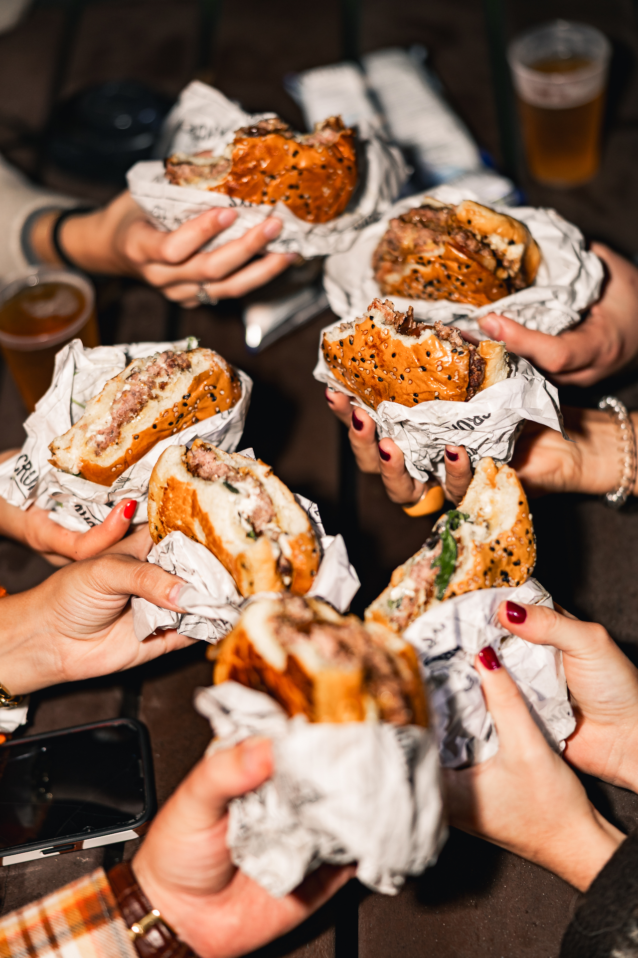 Grupo de amigos a partilhar hambúrgueres Crunchy's num evento à noite, embrulhados em papel da marca